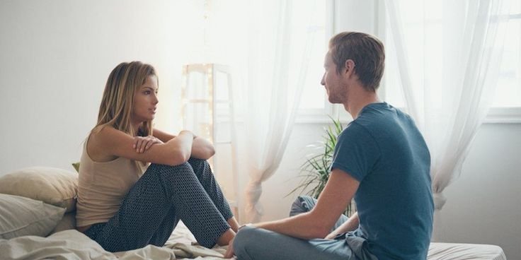 Couple having an open conversation about using condoms to enhance mutual climax, focusing on trust and communication in a private space.