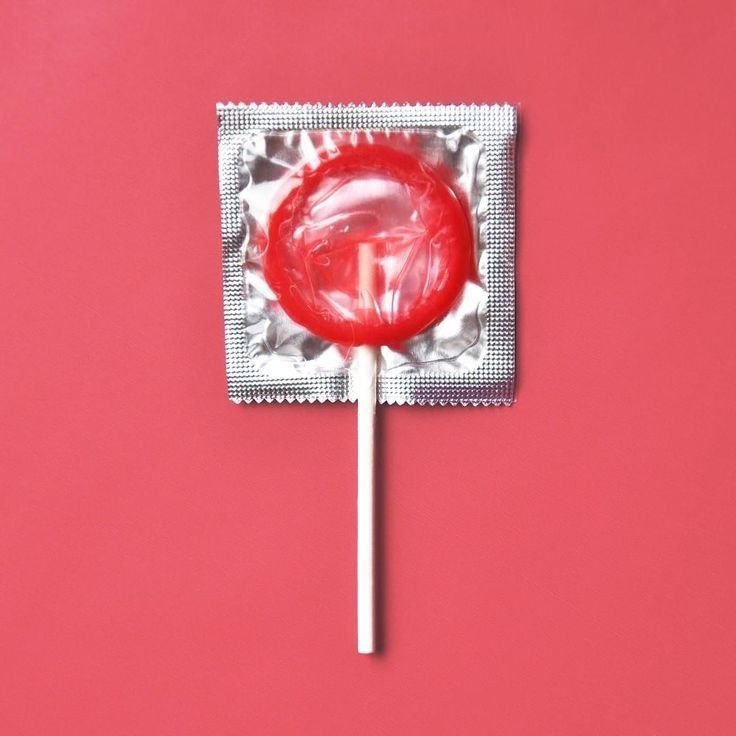 Red lollipop wrapped in foil packaging resembling a condom, symbolizing protection and playfulness in Mutual Climax products.