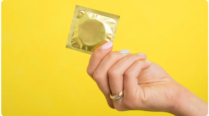 Hand holding a gold condom packet, symbolizing protection and support for Mutual Climax